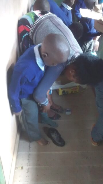 The teacher helping Opiyo to try on his new shoe
